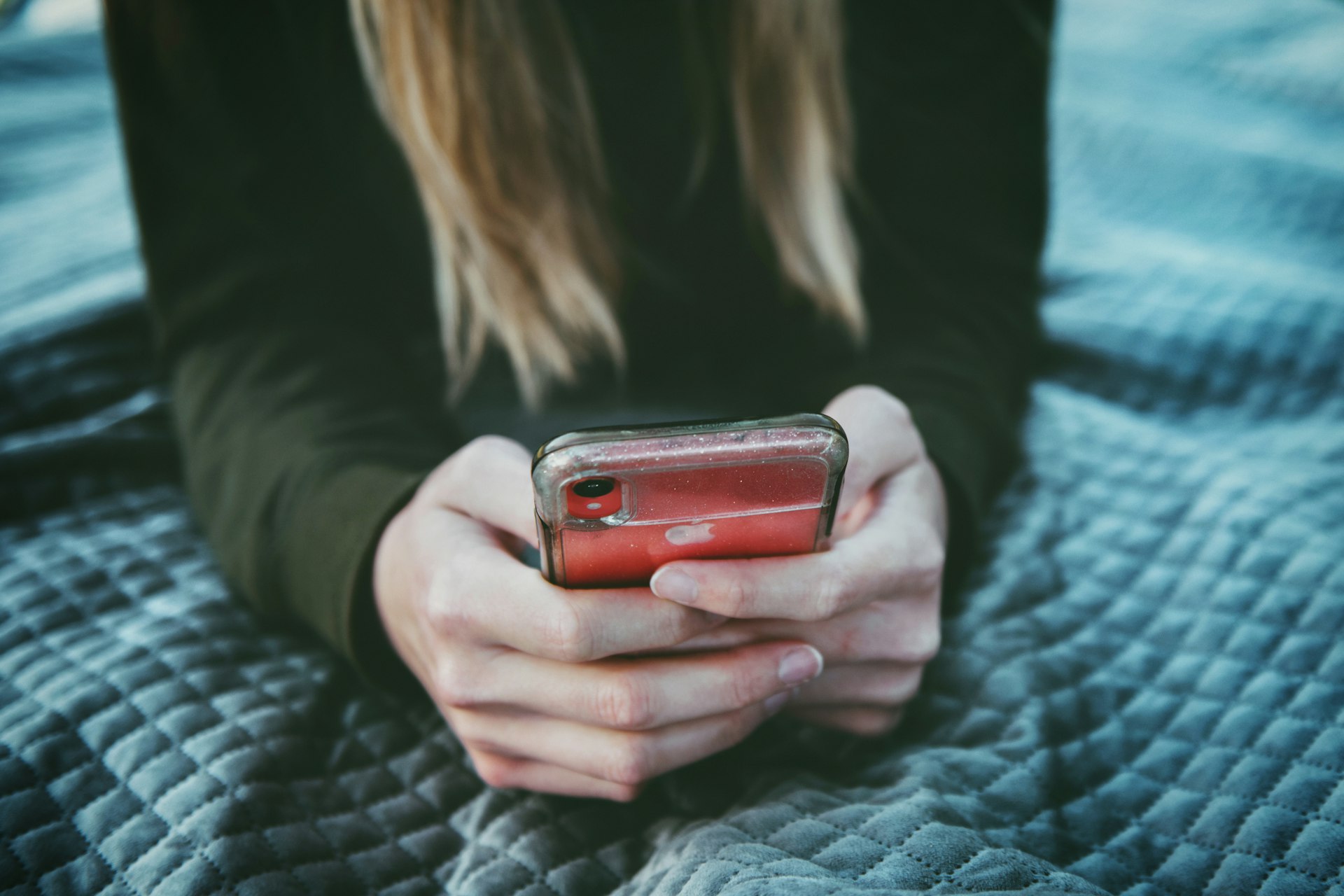 A woman is texting on a red and silver phone.